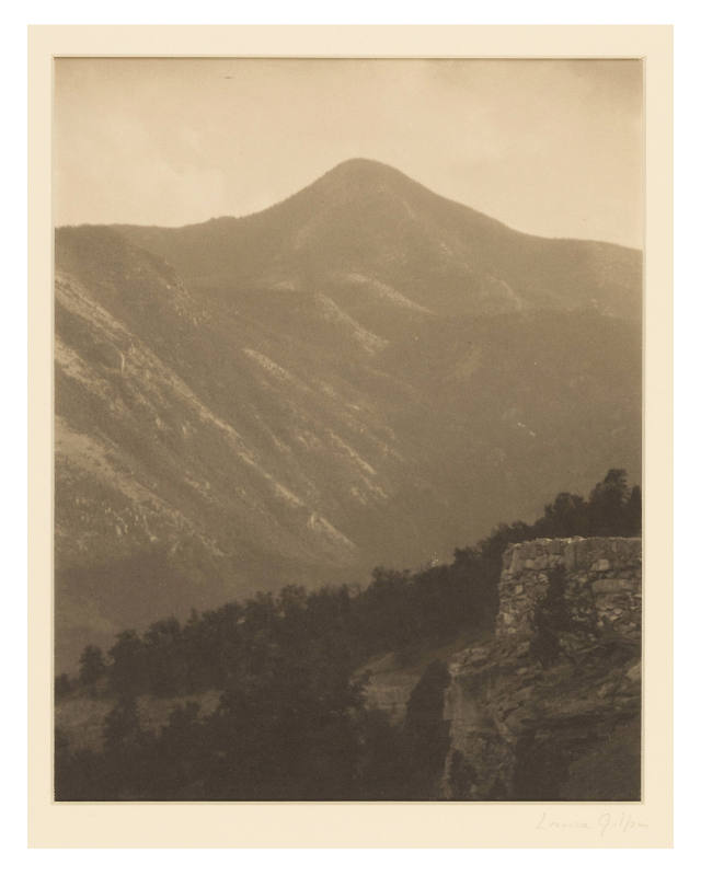 Greyscale photograph of a mountain with a stone structure in the lower right