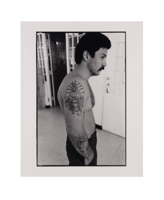 Black and white photo of  a shirtless person's profile with a tattoo on their arm