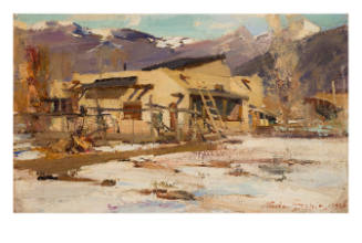 Adobe house surrounded by melting snow in front of mountains and brown bare trees

