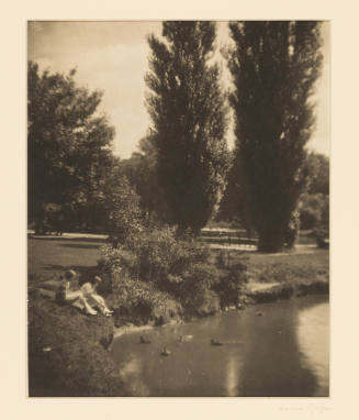 Greyscale photograph of a park with two people sitting beside a pond with ducks