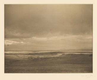 Greyscale photograph of a flat, open field under a cloudy sky 