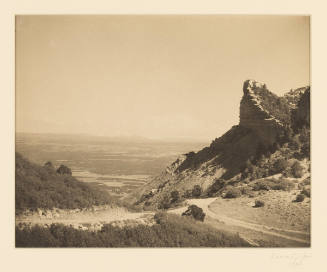 Greyscale photograph of two dirt roads connecting to go through rock formations into a valley