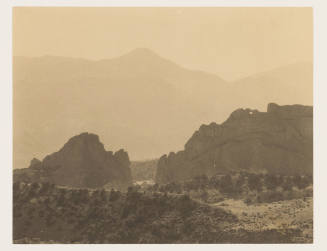 Greyscale photograph of large, flat rock formations with hazy mountains in the background 