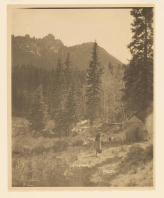 Greyscale photograph of two individuals at a campsite with tall mountains in the backgroud