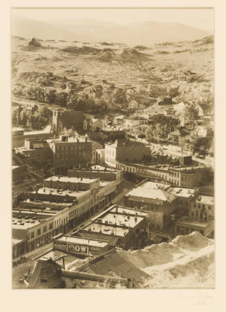 Greyscale photograph looking down at a small city with mountains in the background