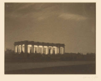 Greyscale photograph taken at dusk of an open-air memorial building with interior lighting