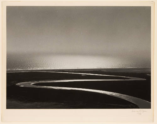 Greyscale photograph of a river winding to a larger body of water meeting the sky