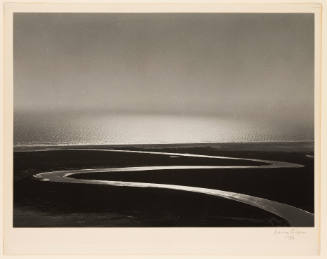 Greyscale photograph of a river winding to a larger body of water meeting the sky