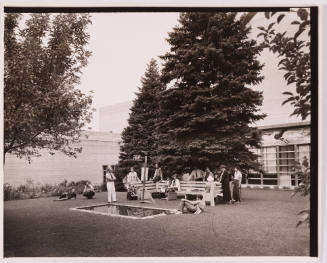 Greyscale photograph of a group gathered beside an easel and a square pond in a courtyard